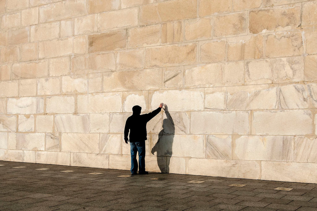 Horizontal color photograph of a person wearing a hoodie sweatshirt reaches out to touch the Washington Monument. Washington, D.C.